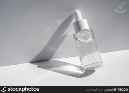 A white transparent bottle with serum in the rays of the sun. Laconic bottle shape.. A white transparent bottle with serum in the rays of the sun.