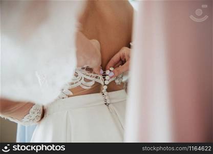 A white wedding dress is knitted to the bride. A bride is being helped to wear the wedding dress. The bride&rsquo;s preparation for the wedding. Bride white lace wedding dress. Bride help put on the wedding dress