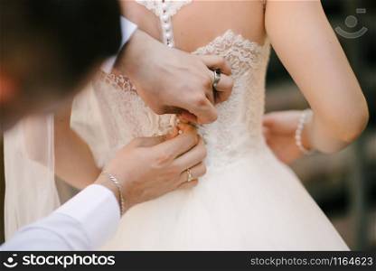 A white wedding dress is knitted to the bride. A bride is being helped to wear the wedding dress. The bride&rsquo;s preparation for the wedding. Bride white lace wedding dress. Bride help put on the wedding dress