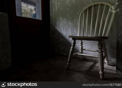 A white wooden chair standing in an empty room under the light from the door. Selective focus.