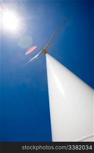 A wind turbine and the sun against a deep blue sky. Image has heavy lens flare from the sun.