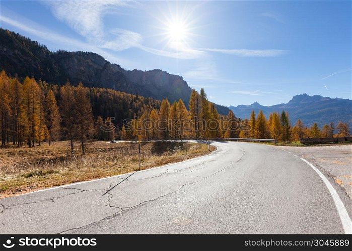 A winding asphalt road curves through autumn trees and mountains. Alpine mountain landscape. A winding road curves through autumn trees in New England