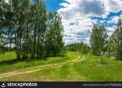 A winding dirt road by the river on a sunny summer day, Russia.