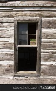 A window on an old, weathered barn that is surrounded by rough-hewn wood planks. There is a view through some missing glass to the other side. Note the building (and window frame) has gone slightly askew over the years.