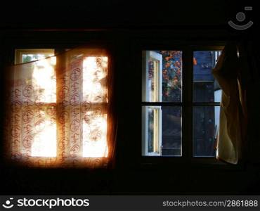 A window with curtain illuminted by sun, and a window without