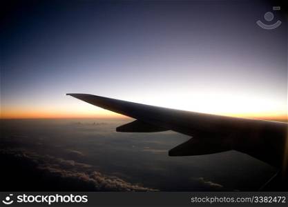 A wing on an airplane in flight at sunset