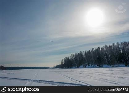 A winter landscape with a helicopter in the backlight. The sun illuminates the snow-covered river.