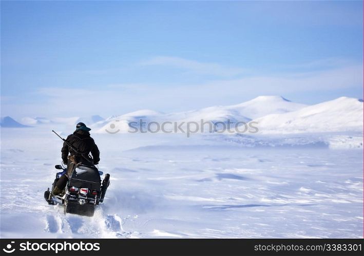 A winter landscape with a snowmobile travelling across frozen ice