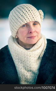 A winter portrait of a senior adult woman wearing a wool cap and a scarf, with a snow background