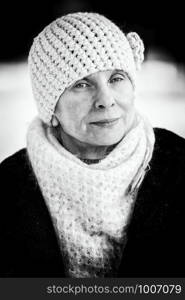 A winter portrait of a senior adult woman wearing a wool cap and a scarf, with a snow background