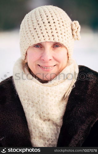 A winter portrait of a smiling senior adult woman wearing a wool cap and a scarf, with a snow background