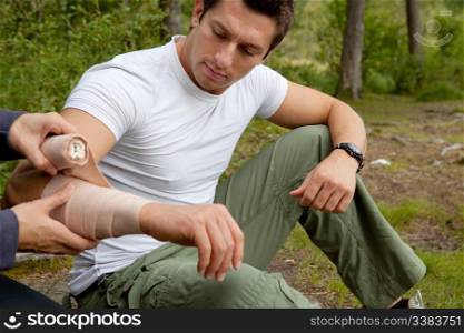 A woman applying an arm bandage on a male camper - focus on male face