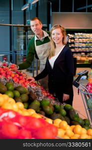 A woman buying fruit and vegetables at a supermarket, receiving help from a grocer