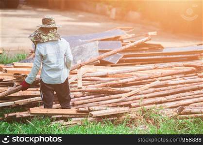A woman construction laborer carrying wood beam on green grass.