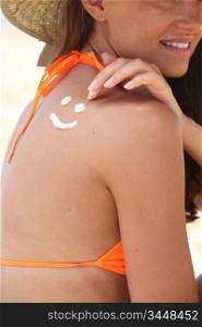 a woman drawing a face on her back with suntan lotion