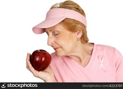 A woman dressed in pink with breast cancer awareness ribbon, smelling delicious red apple. Emphasizes healthy eating to beat cancer. Isolated on white.