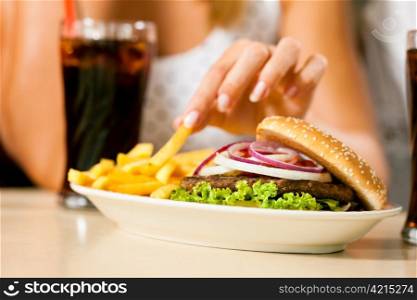 A woman eating hamburger and drinking soda in a fast food diner; focus on the meal