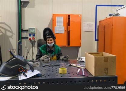 A woman employed in a modern factory for the production and processing of metals in a work uniform welds metal materials. High quality photo. A woman employed in a modern factory for the production and processing of metals in a work uniform welds metal materials