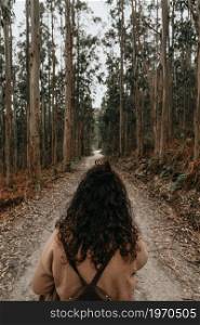 A woman facing a long infinite path in the middle of the forest