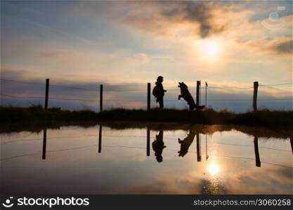 A woman gives a cookie to her dog during a walk in the mountains at sunset