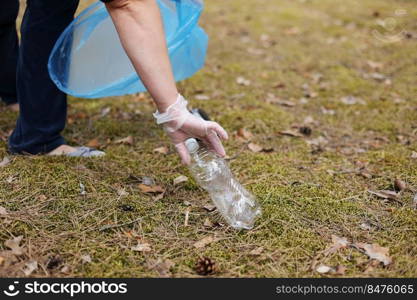 A woman hands in gloves collects and puts used plastic bottle into a blue trash bag. A volunteer cleans up the park on a sunny bright day. Clearing, pollution, ecology and plastic concept.. A woman hands in gloves collects and puts used plastic bottle into a blue trash bag. A volunteer cleans up the park on a sunny bright day. Clearing, pollution, ecology and plastic concept