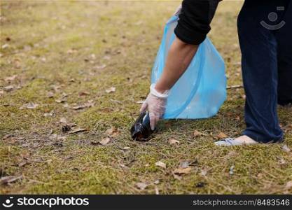 A woman hands in gloves collects and puts used plastic bottle into a blue trash bag. A volunteer cleans up the park on a sunny bright day. Clearing, pollution, ecology and plastic concept.. A woman hands in gloves collects and puts used plastic bottle into a blue trash bag. A volunteer cleans up the park on a sunny bright day. Clearing, pollution, ecology and plastic concept