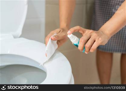 A woman hands with alcohol spray and wet wipe cleans a bathroom toilet before using. Protection against infectious virus, bacteria and germs, Coronavirus/ Covid-19, health care concept.