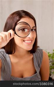 A woman holding a magnifying glass in front of her eye and looking at the camera