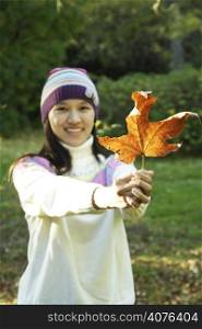 A woman holding an autumn leaf (focus on leaf, rather shallow DOF)