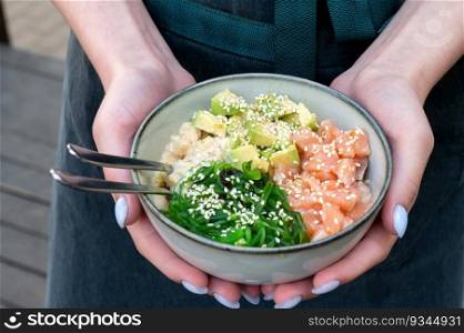 A woman holds a traditional Hawaiian bowling poker in her hands. Hawaiian and Japanese cuisine. Healthy food. poke bowl with seaweed, avocado, cucumber, salmon, sesame. A woman holds a traditional Hawaiian poke bowl with fish in her hands. Hawaiian and Japanese cuisine