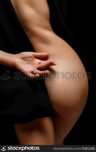 a woman in a black jacket on a naked body posing on a black background covering her buttocks