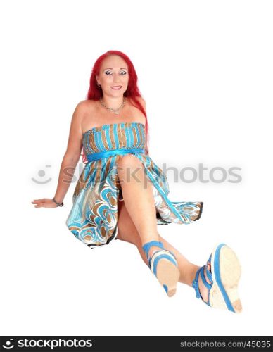 A woman in a dress and heels with long red hair sitting on the floor,smiling, isolated for white background.