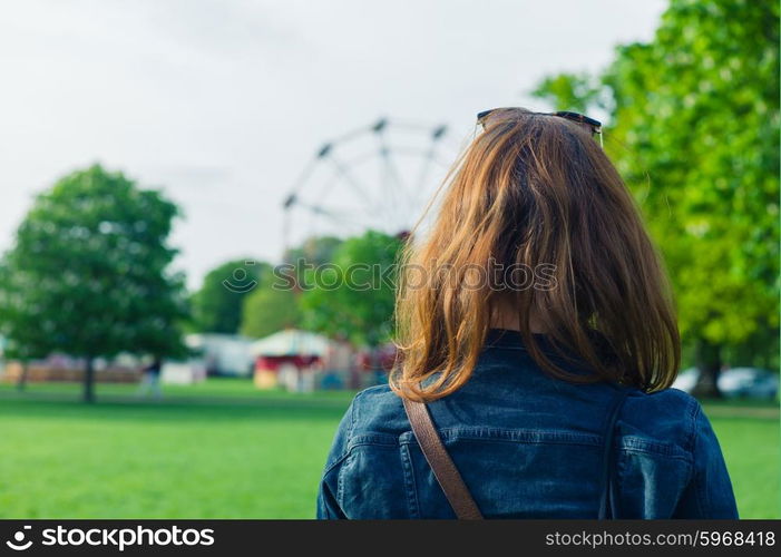 A woman in a park is looking at a fun fair