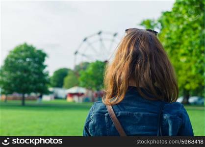A woman in a park is looking at a fun fair