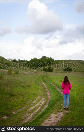 A woman in a pink raincoat looks at a mountain road. The concept of hiking in the mountains, trekking, outdoor recreation. A woman in a pink raincoat looks at a mountain road. The concept of hiking in the mountains, trekking, outdoor recreation.