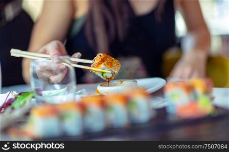 A woman in a restaurant dines sushi, dunks a slice of rolls in soy sauce, trendy Asian food, a tasty dietary dish