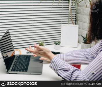 a woman in a striped shirt sits at a white desk and communicates online via a laptop. Video call, blogging. Man actively gesticulates with his hands