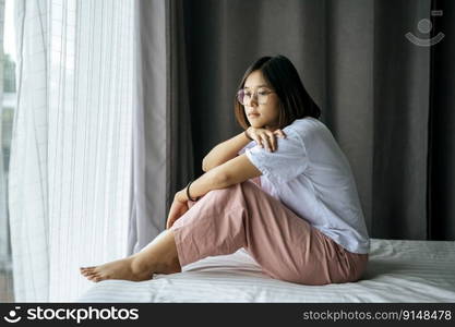 A woman in a white shirt sitting on the bed and looking out.