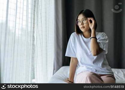 A woman in a white shirt sitting on the bed and looking out.