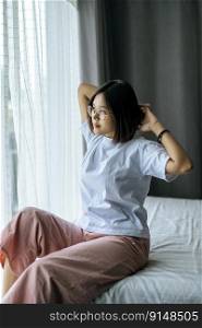 A woman in a white shirt sitting on the bed and raising both arms.