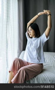 A woman in a white shirt sitting on the bed and raising both arms.