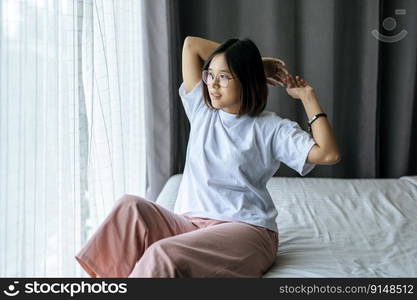 A woman in a white shirt sitting on the bed and raising both arms.