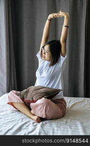 A woman in a white shirt sitting on the bed and raising both arms.