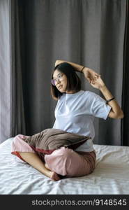 A woman in a white shirt sitting on the bed and raising both arms.