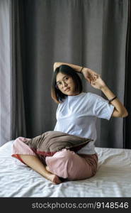 A woman in a white shirt sitting on the bed and raising both arms.