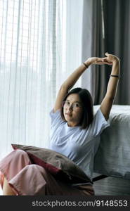 A woman in a white shirt sitting on the bed and raising both arms.