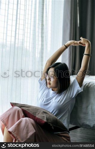 A woman in a white shirt sitting on the bed and raising both arms.
