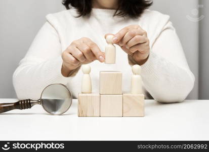 a woman in a white sweater puts a wooden figurine on the podium. The concept of employee search, career advancement. Talented employee