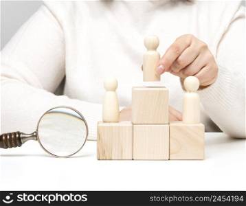 a woman in a white sweater puts a wooden figurine on the podium. The concept of employee search, career advancement. Talented employee