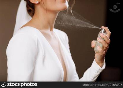 A woman in a white wedding dress gown with a neckline holds a bottle with perfume and splashes on her neck. Morning of the bride in the house, hands without face.. A woman in a white wedding dress gown with a neckline holds a bottle with perfume and splashes on her neck. Morning of the bride in the house, hands without face
